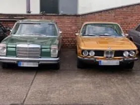 Zwei Oldtimer stehen nebeneinander vor der Werkstatt.