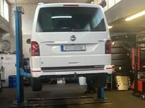 Ein weißer Transporter steht auf einer Hebebühne in der Werkstatt.