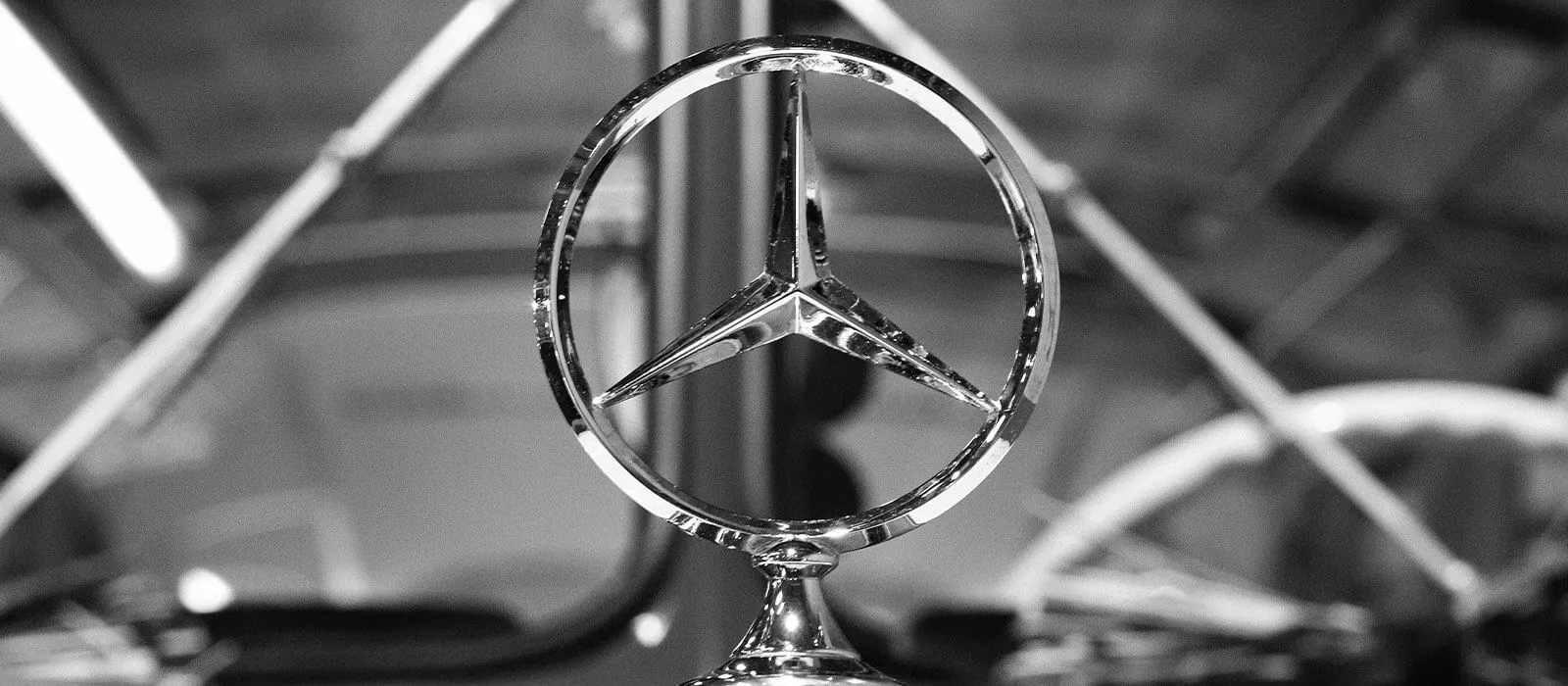 Mercedes-Benz Stern auf der Motorhaube eines Fahrzeugs, Schwarz-Weiß-Aufnahme.
