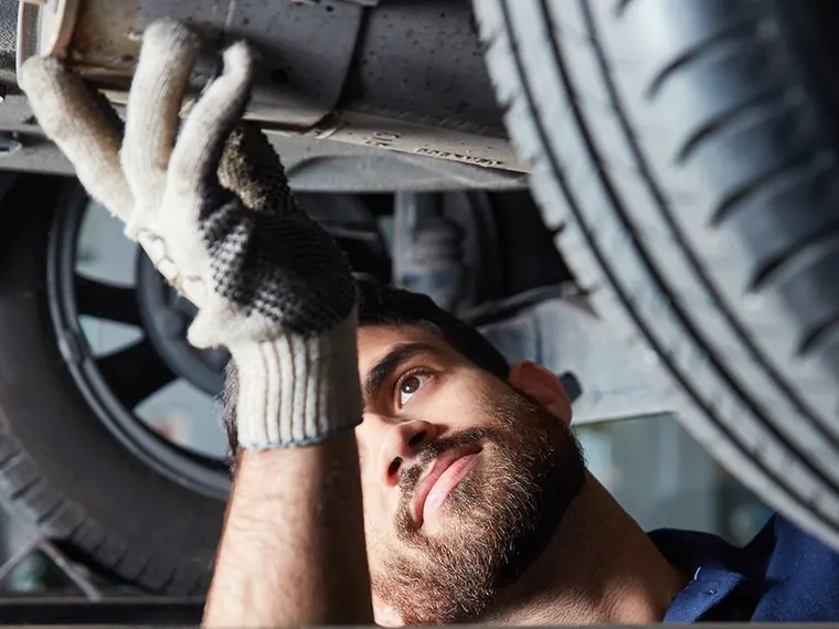Ein Mechaniker arbeitet unter einem angehobenen Fahrzeug an der Radaufhängung.