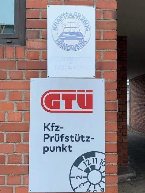 Schild „Kfz-Prüfstützpunkt“ und GTÜ-Logo an der Backsteinwand der Werkstatt.