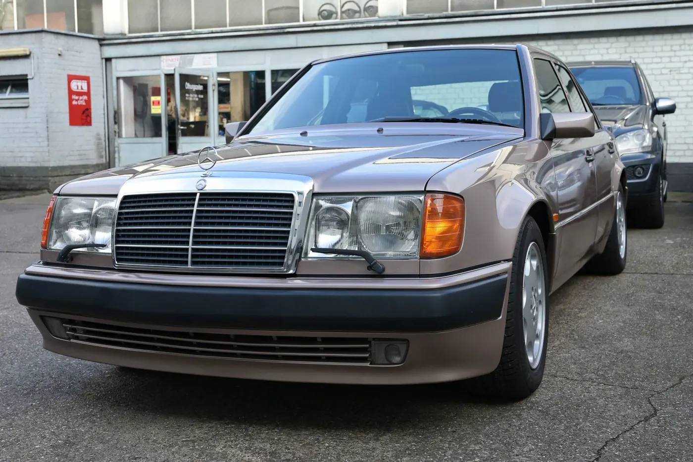 Ein silberner Mercedes-Benz W124 steht vor der Werkstatt in Köln.